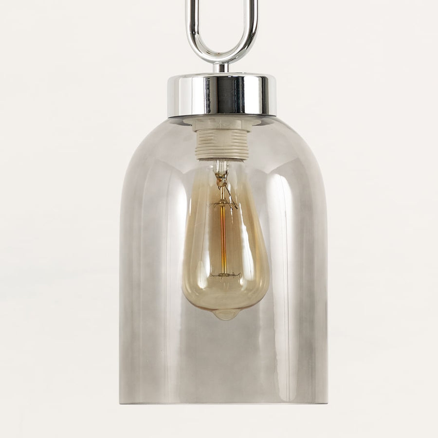 Closeup of smoked glass pendant emphasizing clean contours glossy metal accents and the warm bulb glow for modern aesthetic appeal.