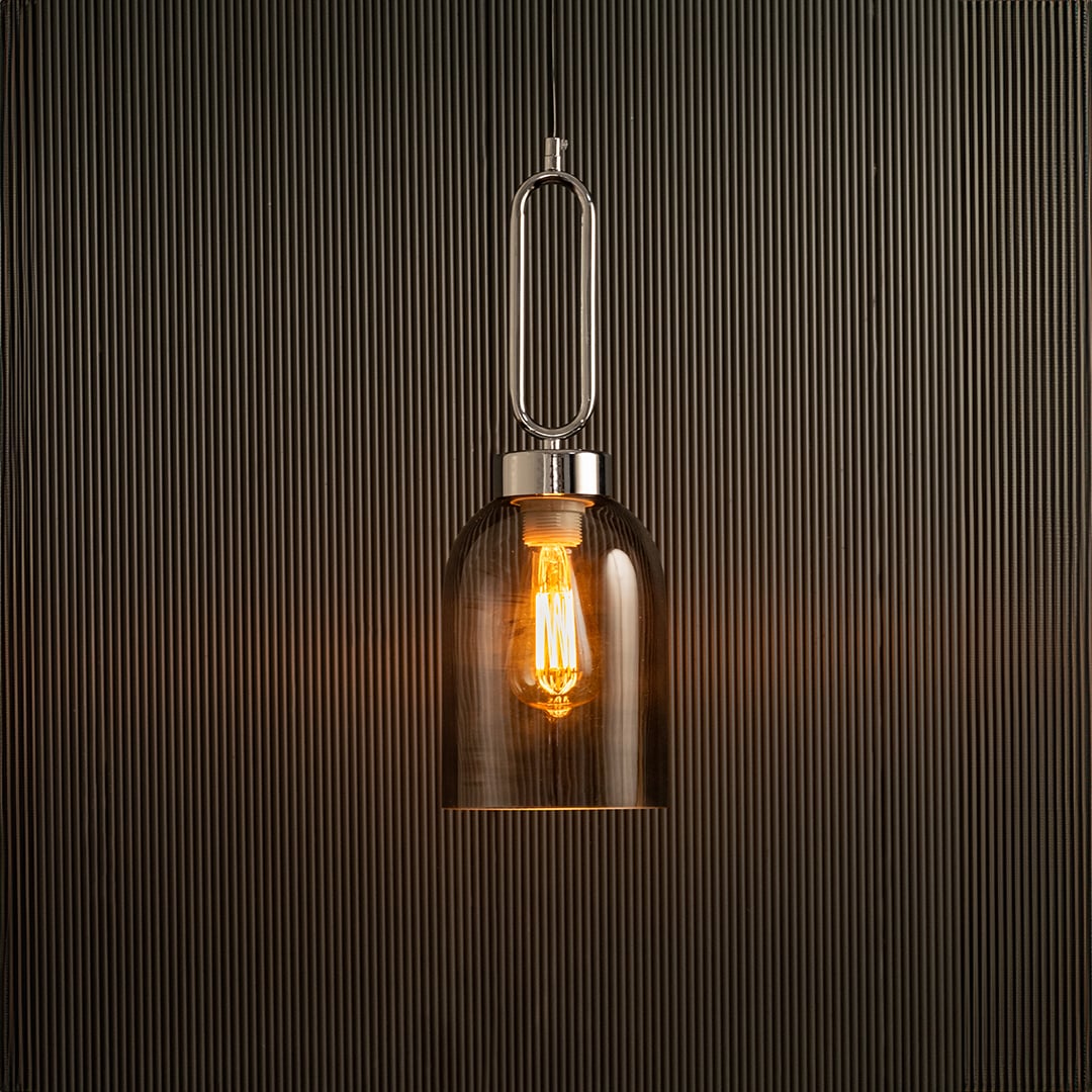 Light on pendant lamp with warm glowing filament inside amber glass shade suspended against textured black wall creating a modern luxury lighting look.