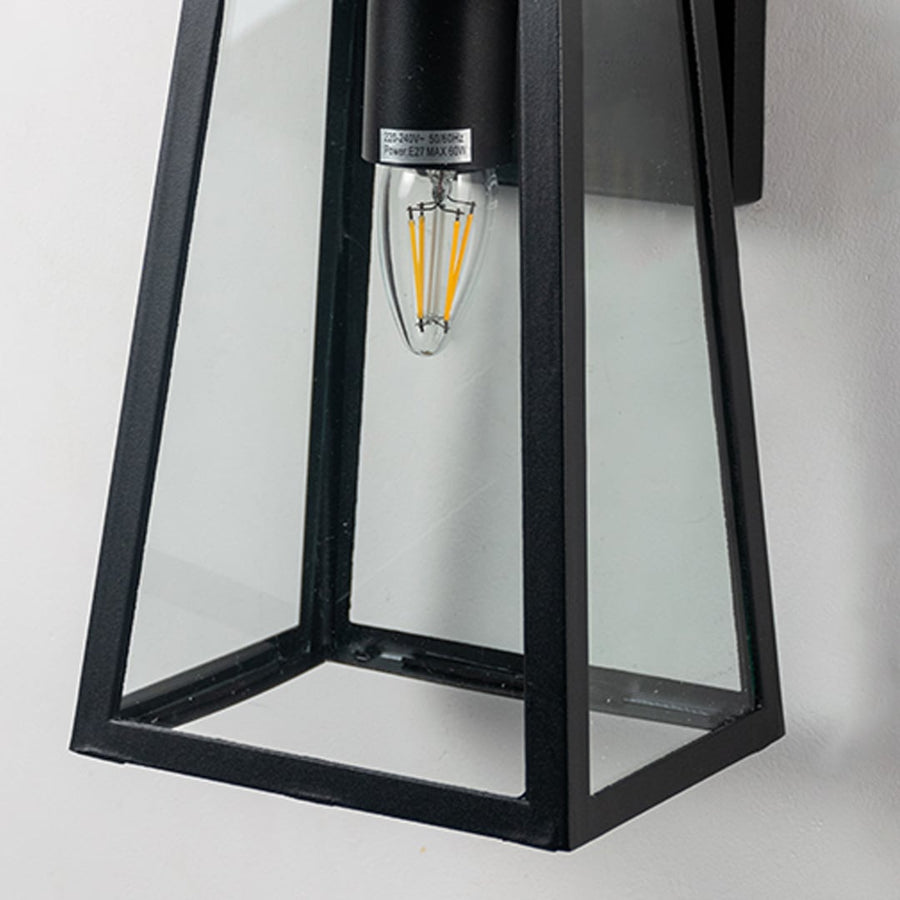 Closeup of black metal outdoor wall light showing clear glass frame and bulb detail for sleek modern exterior design.