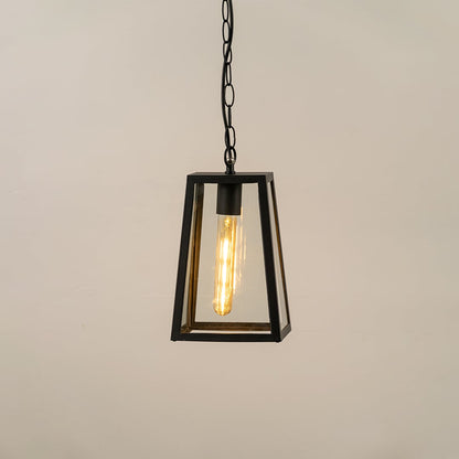 Black modern hanging lantern on white background with light on showing warm glowing filament inside clear tapered glass panels perfect for outdoor ceiling lighting.