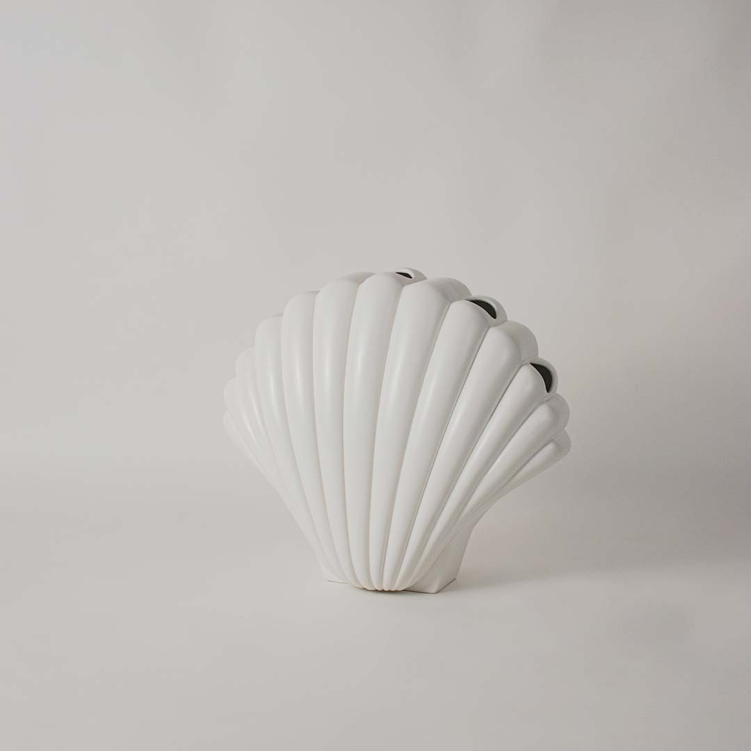 White shell shaped sculpture displayed on a clean white background highlighting its ridged texture and elegant form.