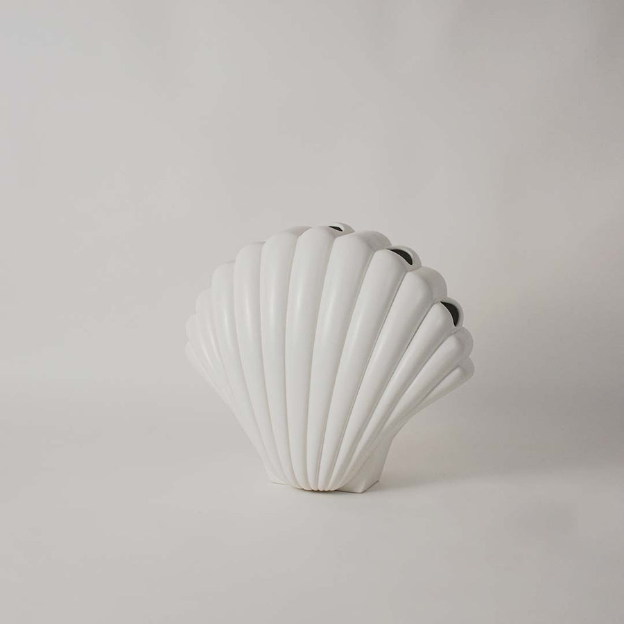 White shell shaped sculpture displayed on a clean white background highlighting its ridged texture and elegant form.