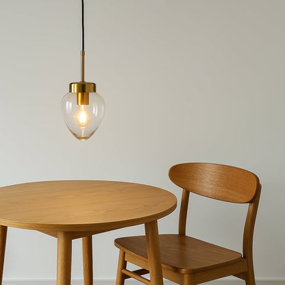 Heart-shaped glass pendant light with warm glow hanging above a light wood dining table and chair in a minimalist room.