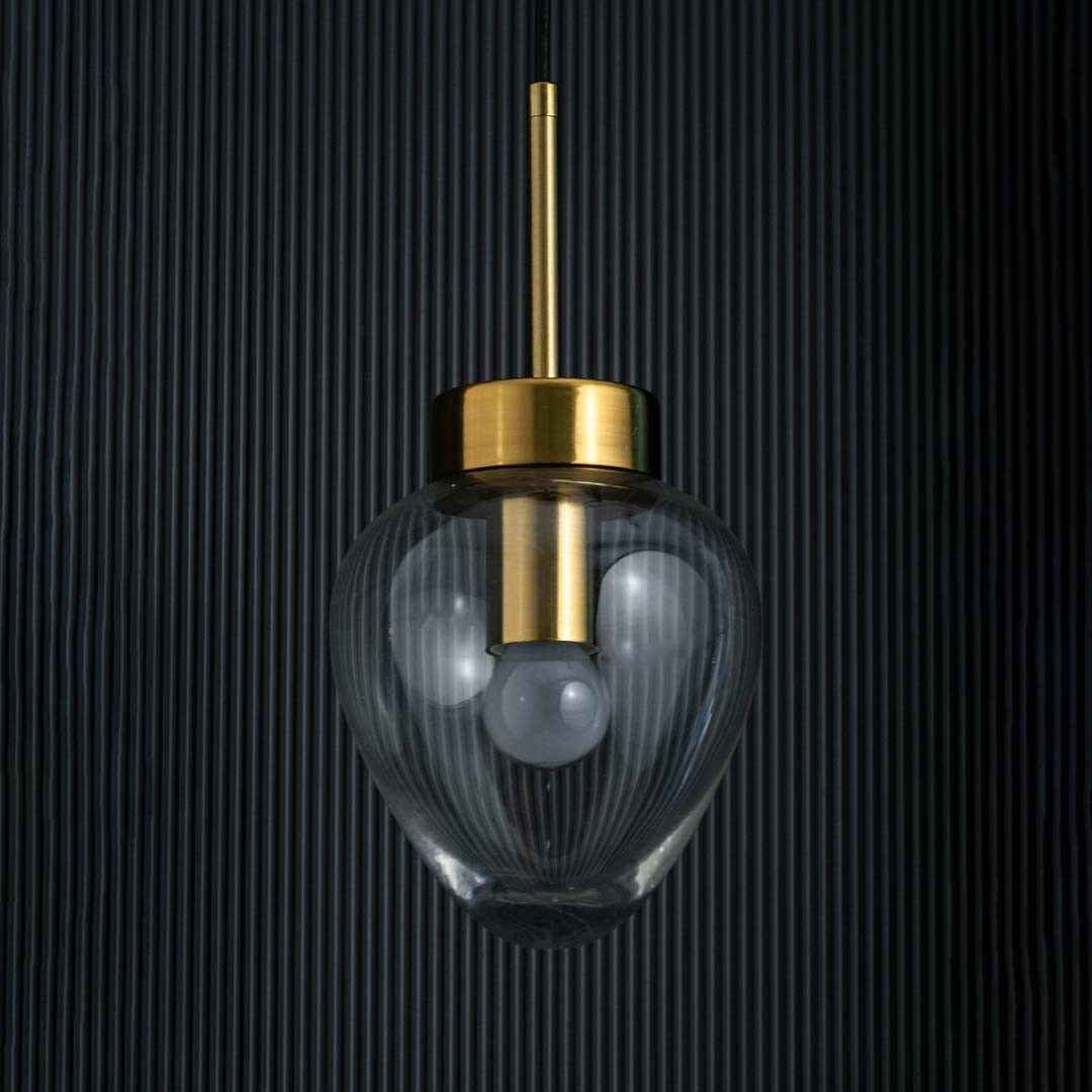 Clear glass heart pendant light turned off with gold top and visible bulb highlighted on a deep black background.