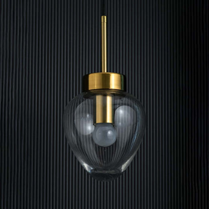 Clear glass heart pendant light turned off with gold top and visible bulb highlighted on a deep black background.