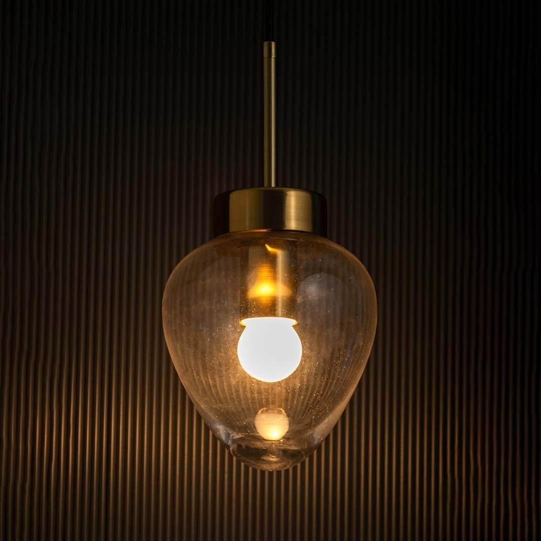 Heart-shaped transparent glass pendant light glowing with gold metal detailing shown against a dark textured background.