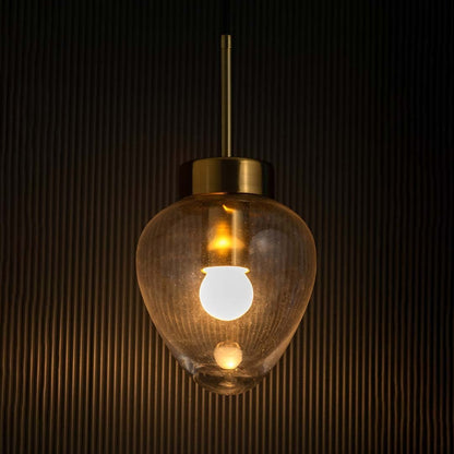 Heart-shaped transparent glass pendant light glowing with gold metal detailing shown against a dark textured background.