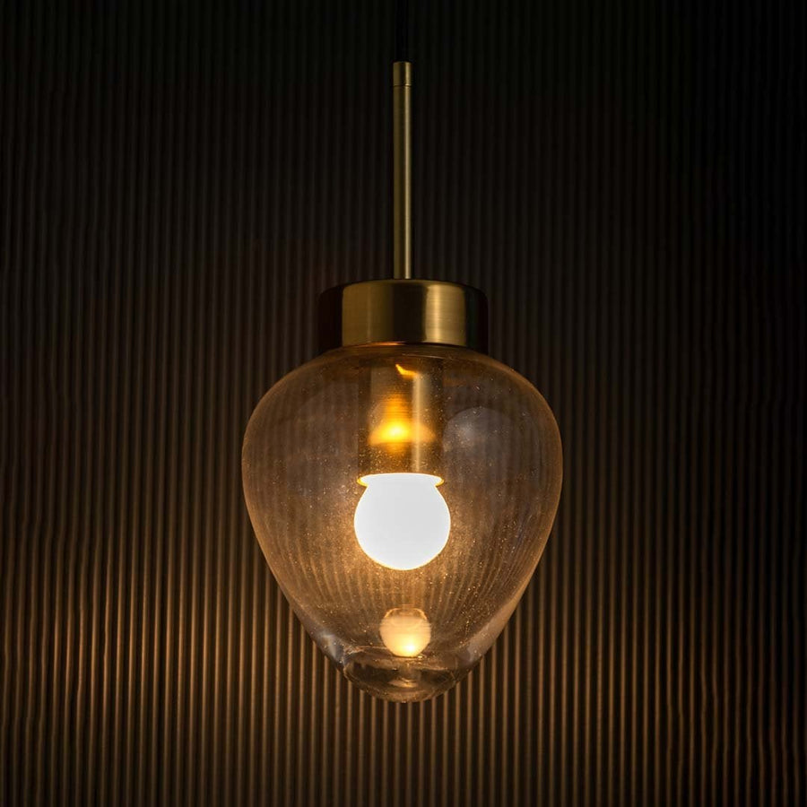 Heart-shaped transparent glass pendant light glowing with gold metal detailing shown against a dark textured background.