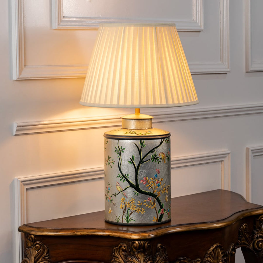 Table lamp on white background showcasing hand painted botanical ceramic base styled with an elegant pleated fabric lampshade.