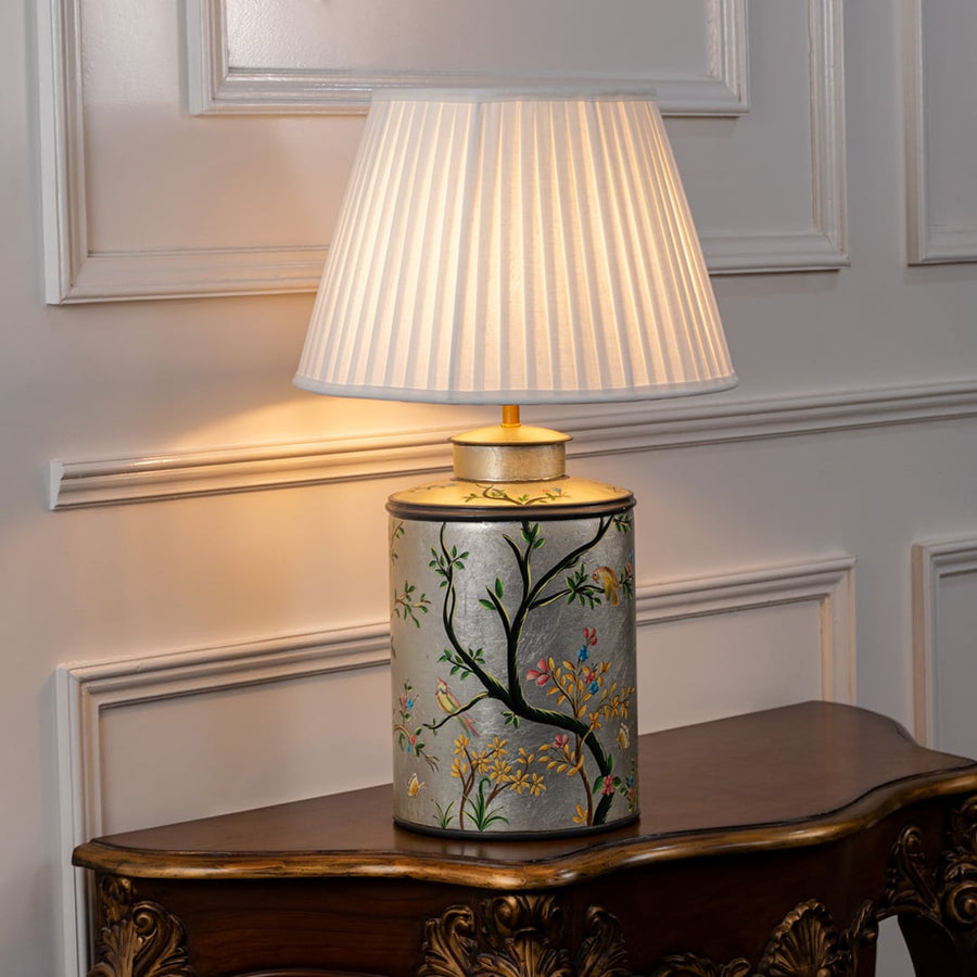Table lamp on white background featuring hand painted botanical ceramic base with birds design paired with a pleated fabric lampshade.