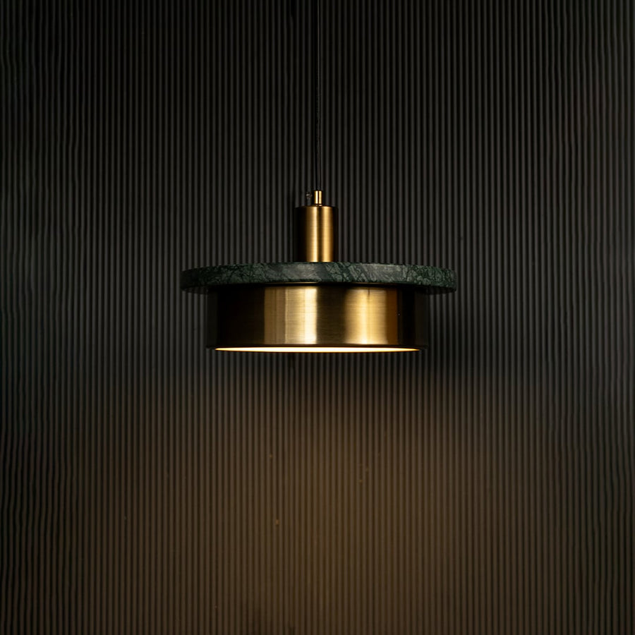 Green marble and metal disc pendant light hanging against dark textured wall with light on for stylish modern décor.