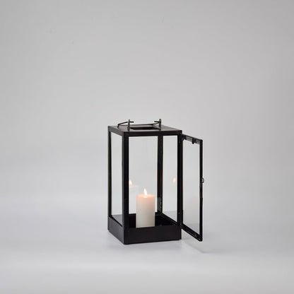 Black metal glass lantern with candle lit shown on white background highlighting warm light classic structure and decor appeal.