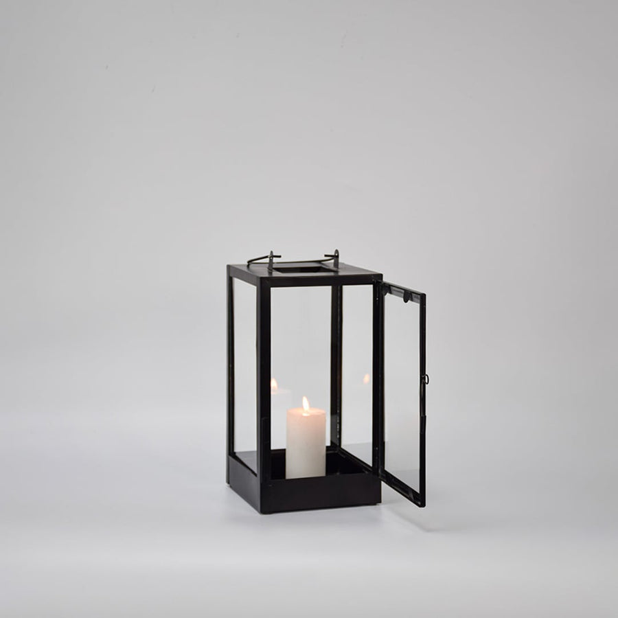 Black metal glass lantern with candle lit shown on white background highlighting warm light classic structure and decor appeal.