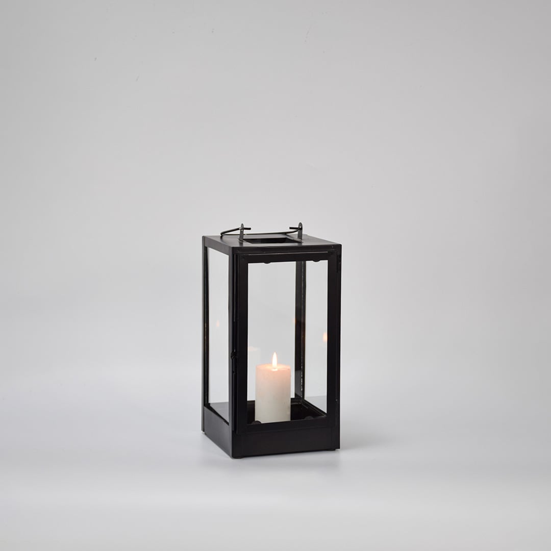 Black metal glass lantern with candle burning on white background emphasizing warm illumination elegant shape and premium look.