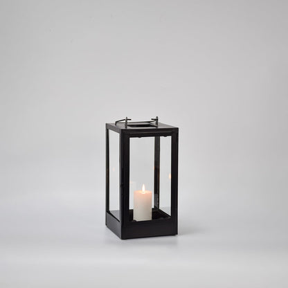 Black metal glass lantern with candle burning on white background emphasizing warm illumination elegant shape and premium look.