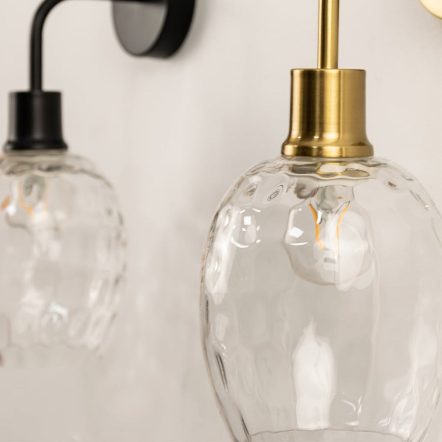 A closeup of a glowing glass wall light with gold and black metal fittings displayed against a white surface producing gentle reflections and stylish modern décor.