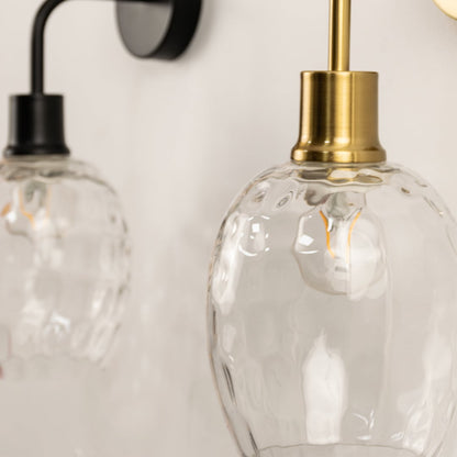 A closeup of a glowing glass and gold metal wall light shown against a soft white background highlighting warm illumination and adding refined contemporary décor.