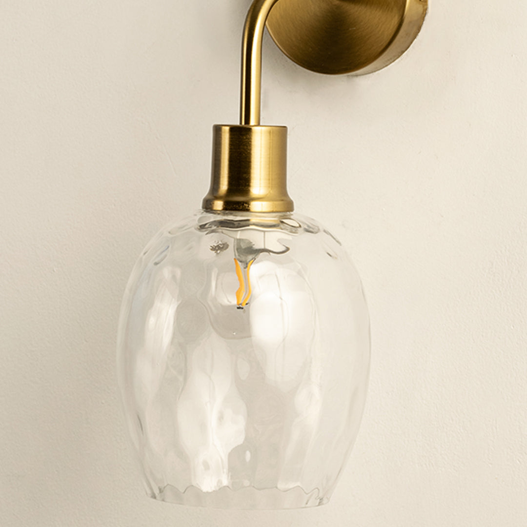 Closeup of gold metal wall light with textured glass shade for elegant modern home interior decor styling.