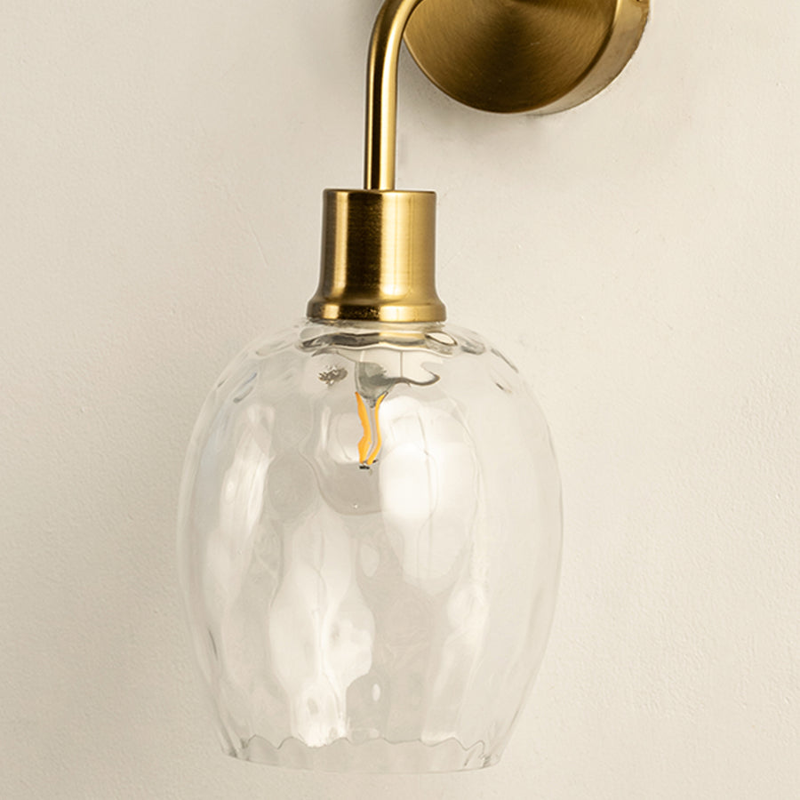 Closeup of gold metal wall light with textured glass shade for elegant modern home interior decor styling.