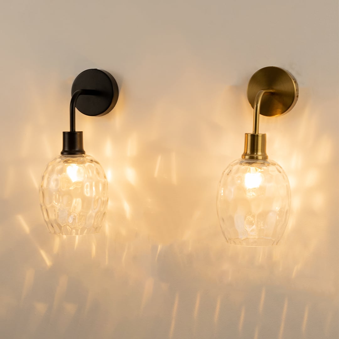 A pair of glowing glass and metal wall lights with sculpted clear shades mounted on a pale wall creating warm patterned illumination and elegant ambient décor.