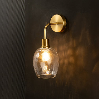 A glowing glass and metal wall light with a warm gold finish mounted on a dark wall creating soft patterned illumination and elegant modern interior décor.