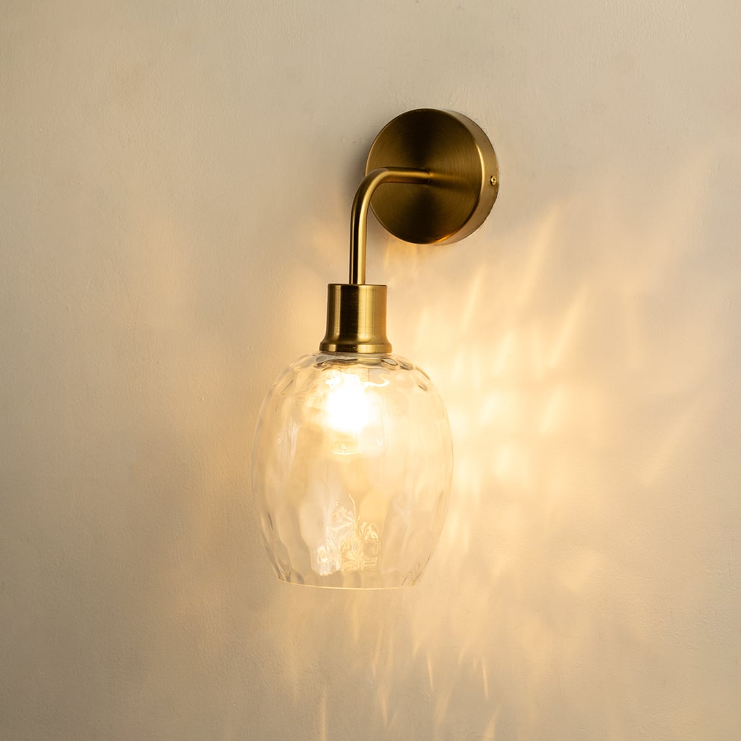 A glowing glass and metal wall light with a sculpted clear shade casting warm patterns on a soft beige wall creating elegant ambient illumination and refined décor.