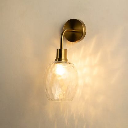 A glowing glass and metal wall light with a sculpted clear shade casting warm patterns on a soft beige wall creating elegant ambient illumination and refined décor.
