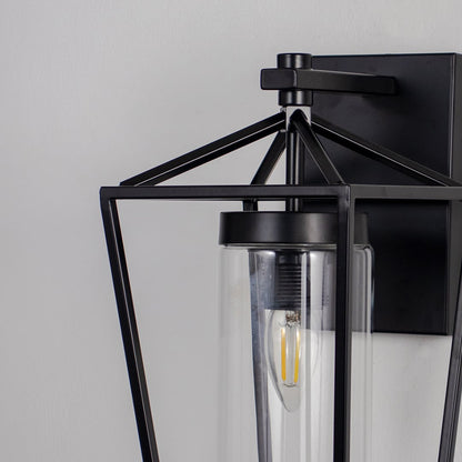 Closeup of black lantern style wall sconce with metal frame and glass shade highlighting exposed filament bulb design.