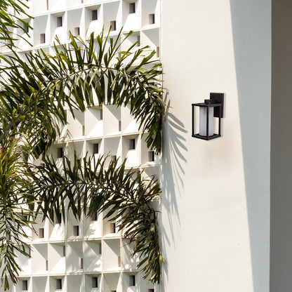 Modern black metal outdoor wall sconce installed on a white villa facade placement near palm trees lifestyle image.