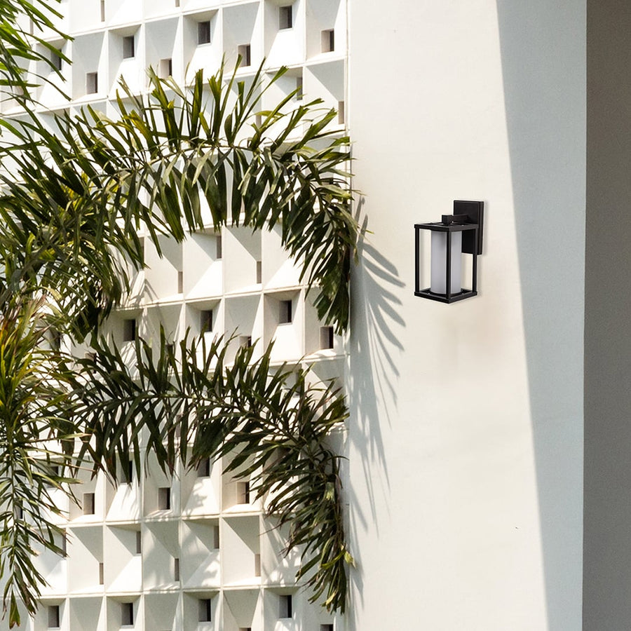 Modern black metal outdoor wall sconce installed on a white villa facade placement near palm trees lifestyle image.