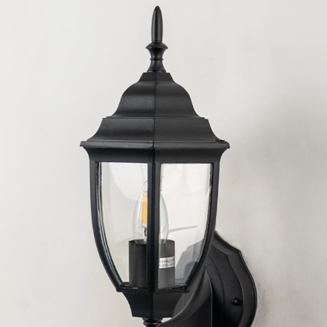 Closeup image of black metal outdoor wall light with clear glass shade for stylish exterior decor.