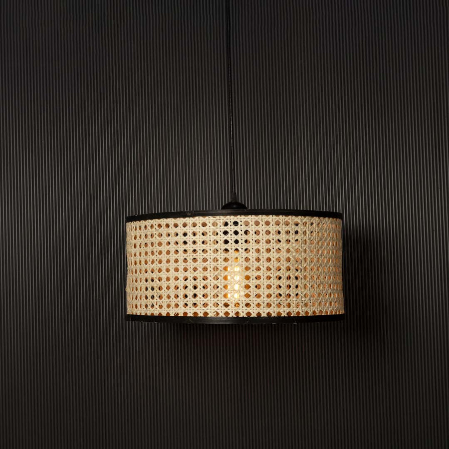 Rattan pendant light glowing through woven cane pattern casting warm ambient light on black background.