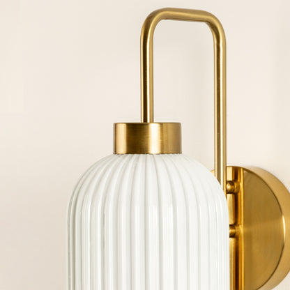 Closeup of gold metal wall light with white ribbed glass shade showcasing detailed texture and premium finish for modern decor styling.