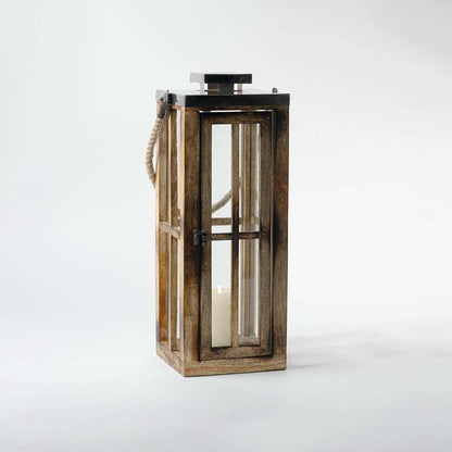 Lit wooden lantern placed on a white background displaying its elegant handcrafted wood frame glass casing and stainless steel lid with rope handle for decorative use.
