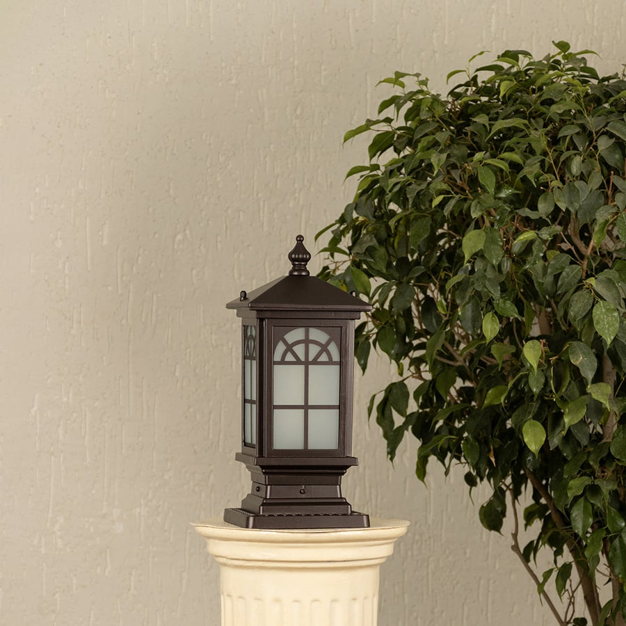 Black outdoor pillar light with ribbed glass Light On placed next to a lush green plant Lifestyle image for modern patio decor.