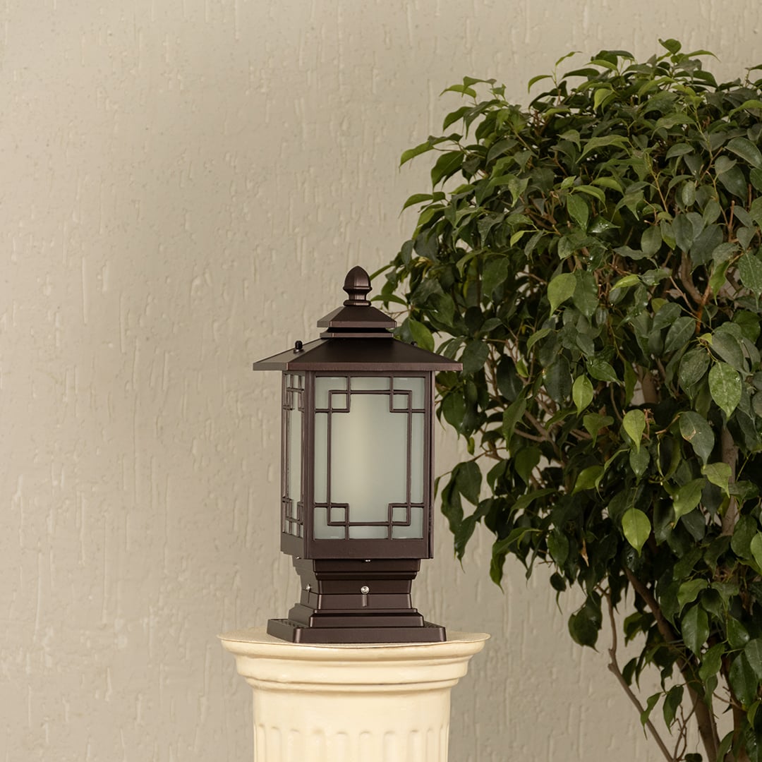 Black outdoor pillar light with ribbed glass Light On placed next to a lush green plant Lifestyle image for modern patio decor.