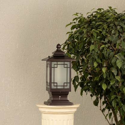 Black outdoor pillar light with ribbed glass Light On placed next to a lush green plant Lifestyle image for modern patio decor.