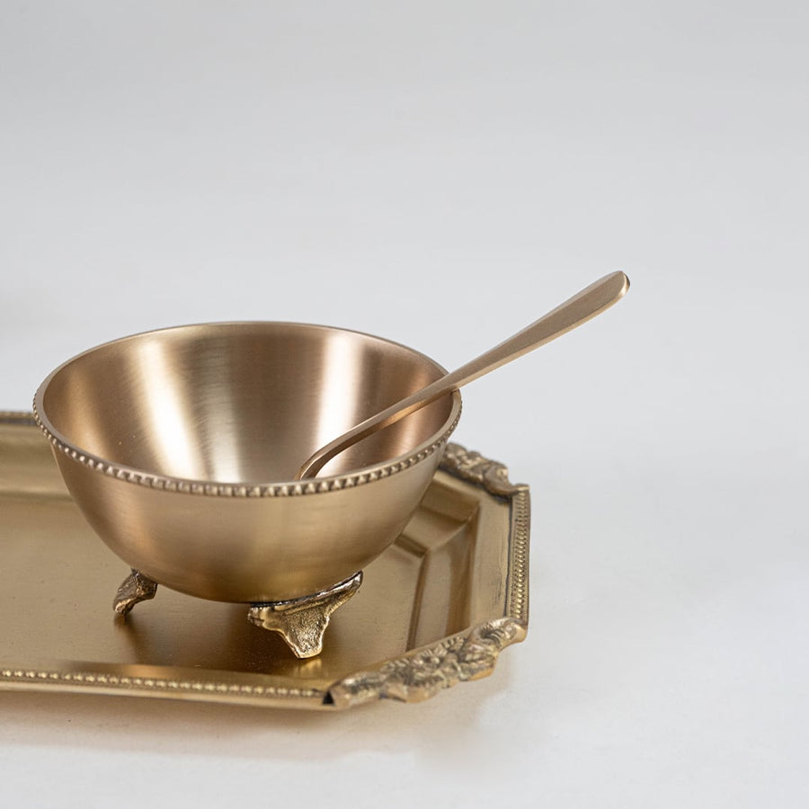Brass snack set with three bowls and spoons arranged on decorative tray placed on a luxurious brown marble surface.