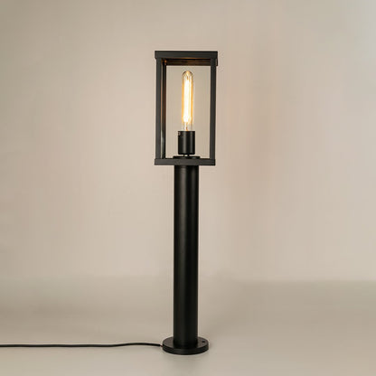 Modern black outdoor bollard light with warm glowing bulb for elegant pathway decor styling use.