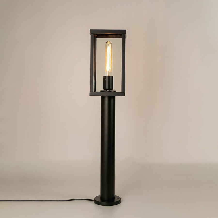 Modern black outdoor bollard light with warm glowing bulb for elegant pathway decor styling use.