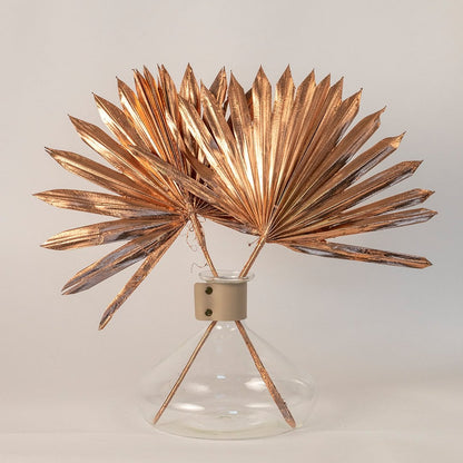 Metallic copper dried palm leaves in glass vase on neutral white background emphasizing minimal and elegant decor style.