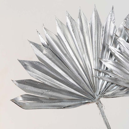 Closeup view of silver palm leaf decor with layered pointed folds showcasing reflective finish and sculptural styling detail.