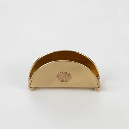 Half-round brass napkin holder with floral crest placed on white background showcasing finish and elegant shape.