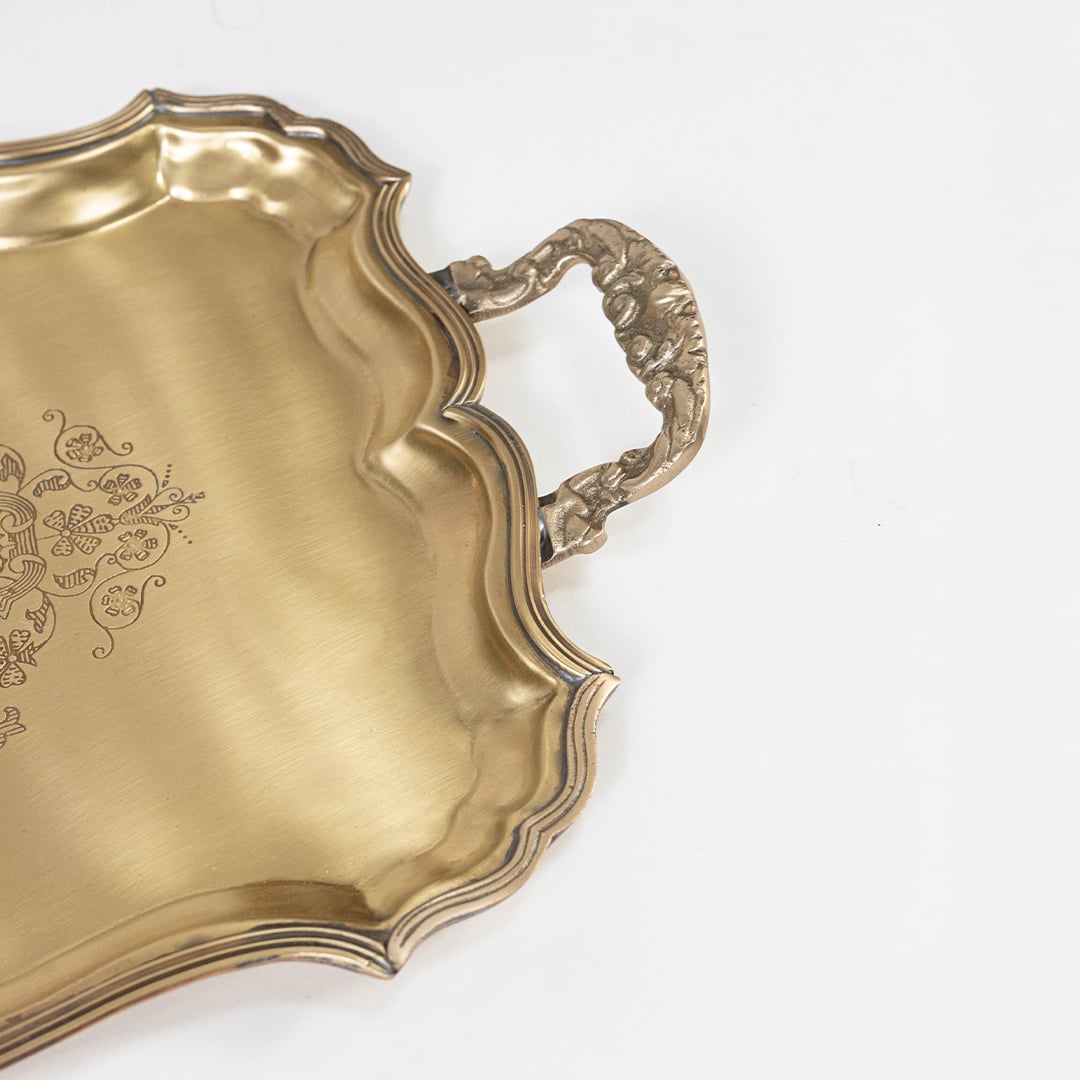 Closeup view of the golden serving tray showing intricate engraved patterns and detailed curved handles.
