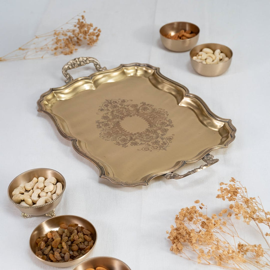Antique brass serving tray with engraved floral motif and elegant handles placed on a plain white studio background.