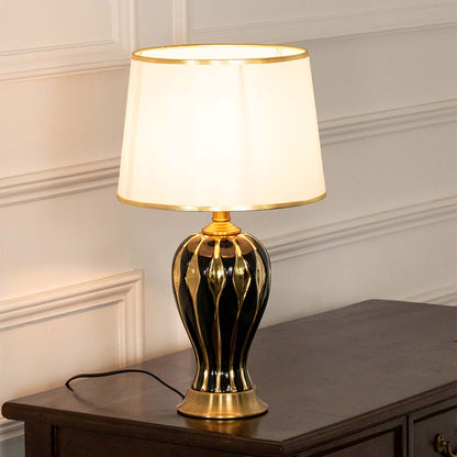 Black ceramic table lamp with fabric shade and gold accents displayed on a console table creating elegant ambient lighting.