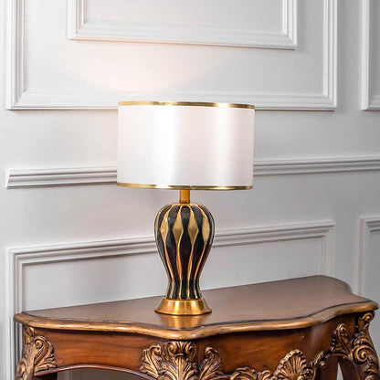 Decorative table lamp with gold metal cage base and white fabric shade on wooden table elegant lighting for bedroom decor.