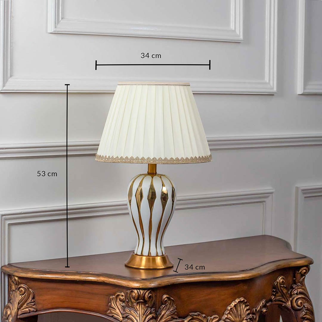 White ceramic table lamp with gold striped base and pleated shade shown with 53cm height and 34cm width.