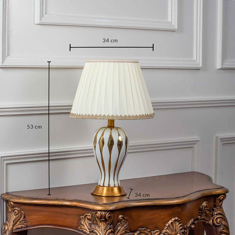 White ceramic table lamp with gold striped base and pleated shade shown with 53cm height and 34cm width.