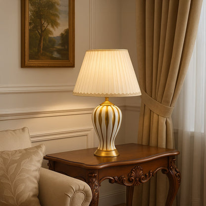 White ceramic table lamp with golden striped base and pleated fabric shade adding classic elegance to living room decor.